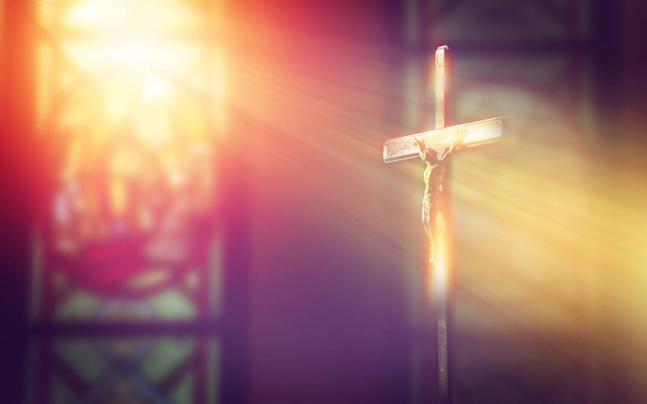 Kruzifix, Jesus am Kreuz in der Kirche mit Lichtstrahlen von Buntglasfenstern.
