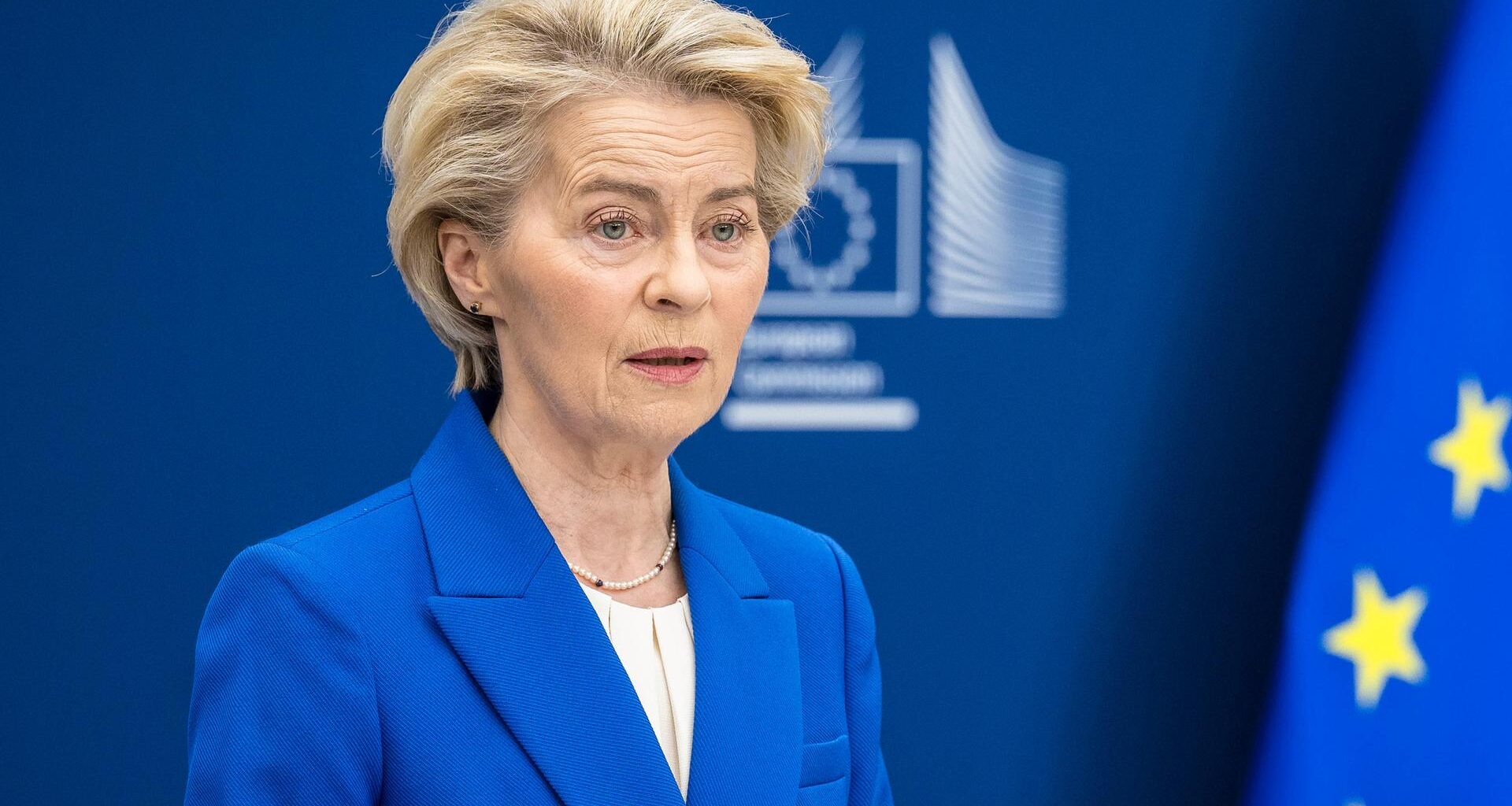 EU-Kommissionspräsidentin Ursula von der Leyen steht in EU-blauem Sakko neben der EU-Flagge an einem Rednerpult