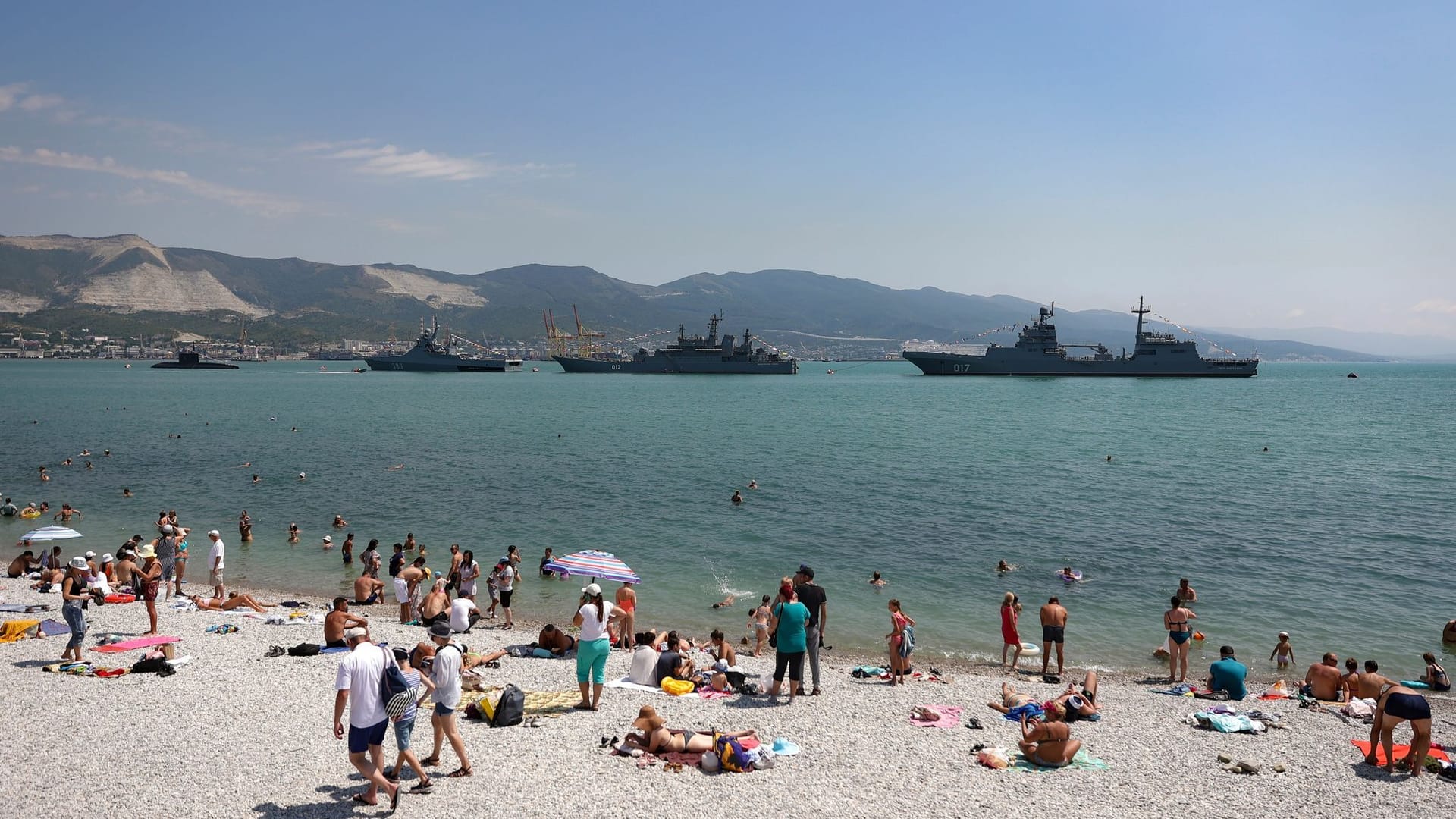 Menschen liegen am Strand, während im Hintergrund Kriegsschiffe anlässlich der Feierlichkeiten zum "Tag der Marine" in Russland im Meer sind. (Archivbild)