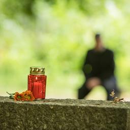 Symbolbild: Eine Grabkerze steht am 25.06.2021 in Berlin auf einem Grabstein, waehrend im Hintergrund ein Mann auf einer Bank sitzt.(Quelle:dpa/C.Klose)