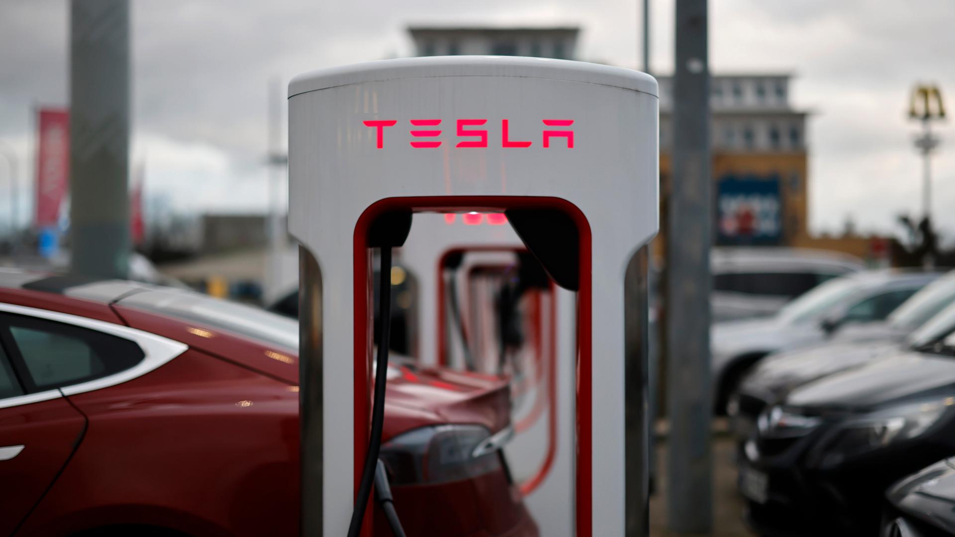 Ladestationen des E-Automobil-Herstellers TESLA für Elektroautos auf einem Parkplatz. Der Schriftzug TESLA leuchtet rot.