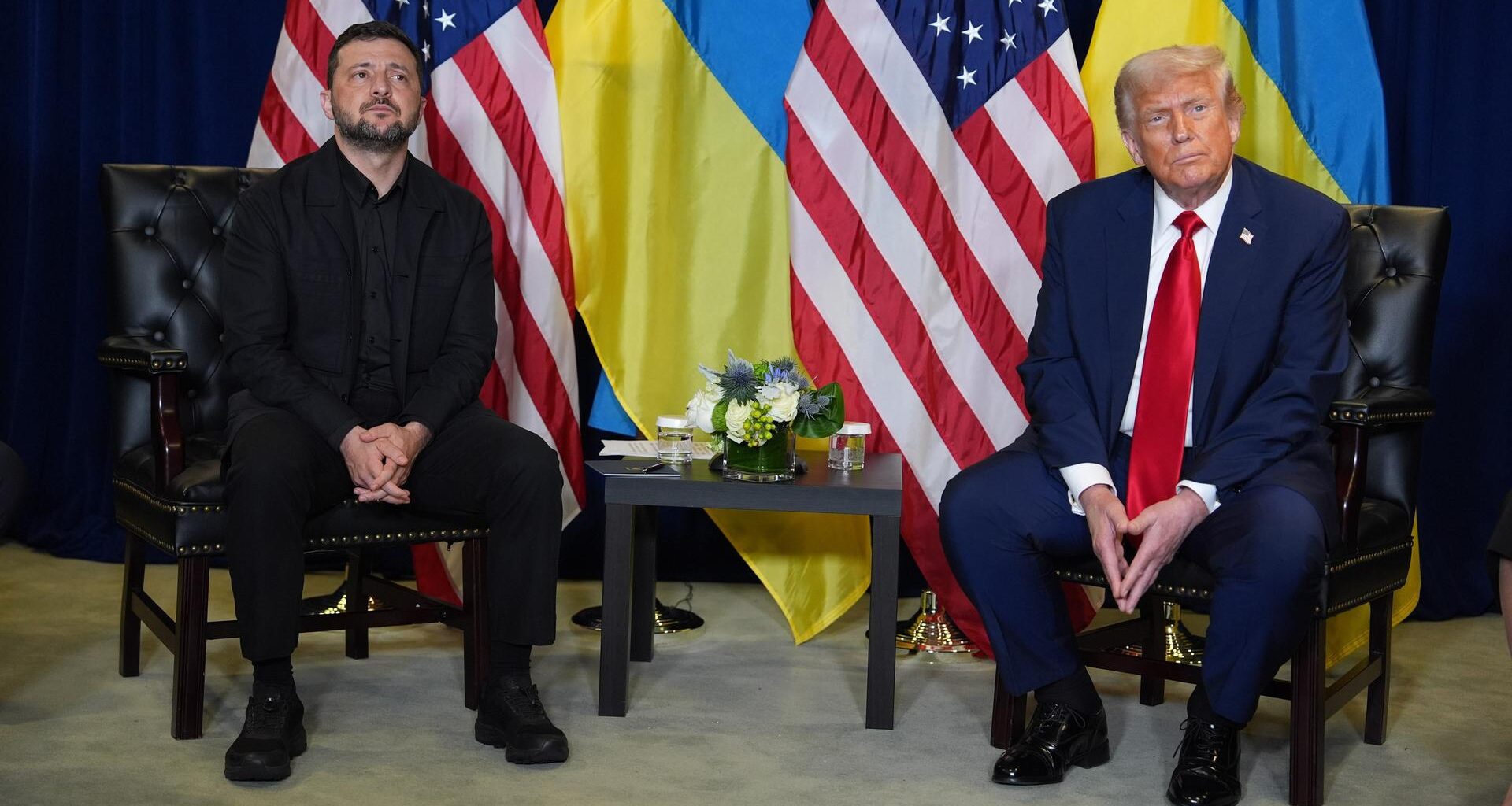 Donald Trump und Wolodymyr Selenskyj sitzen gemeinsam an einem kleinen Tisch. Im Hintergrund sind Flaggen der USA und der Ukraine zu sehen.