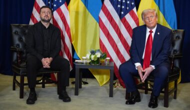Donald Trump und Wolodymyr Selenskyj sitzen gemeinsam an einem kleinen Tisch. Im Hintergrund sind Flaggen der USA und der Ukraine zu sehen.