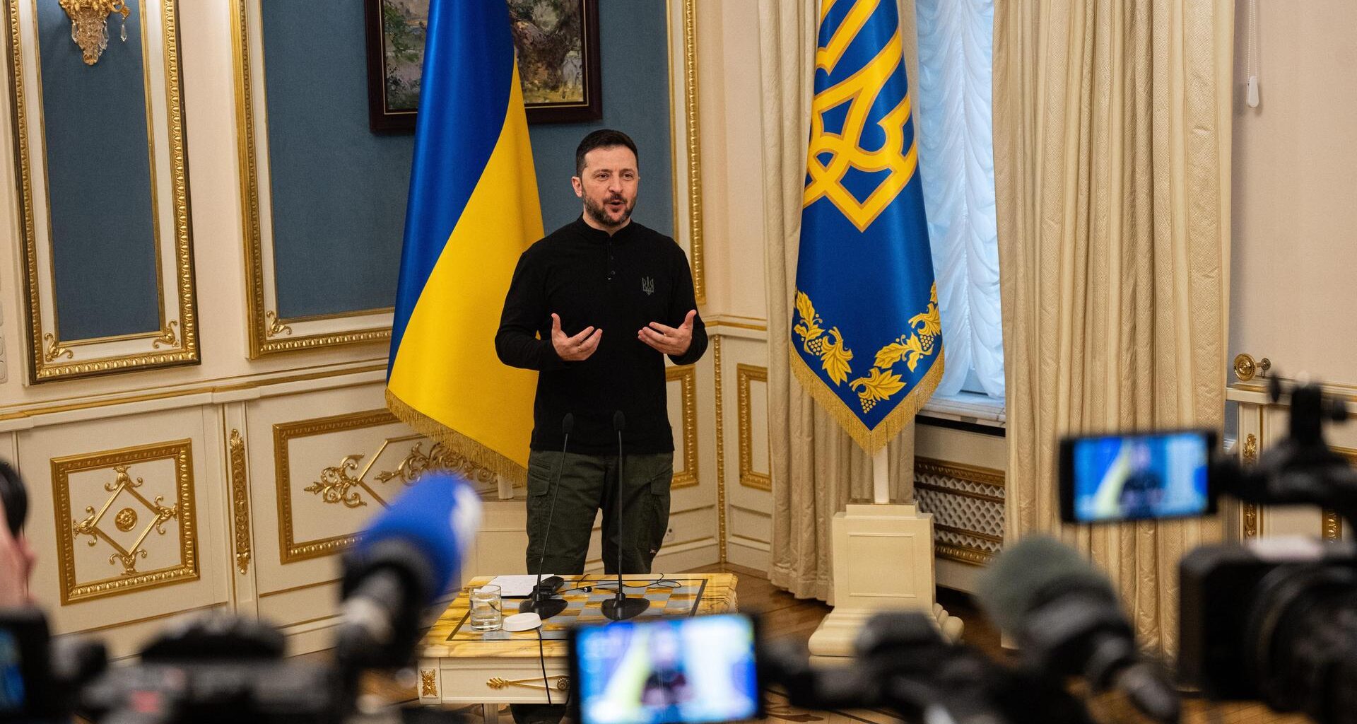 Der ukrainische Präsident Selenskyj steht vor mehreren Pressevertretern und gibt eine Erklärung ab, im Hintergrund sind zwei ukrainische Flaggen zu sehen.