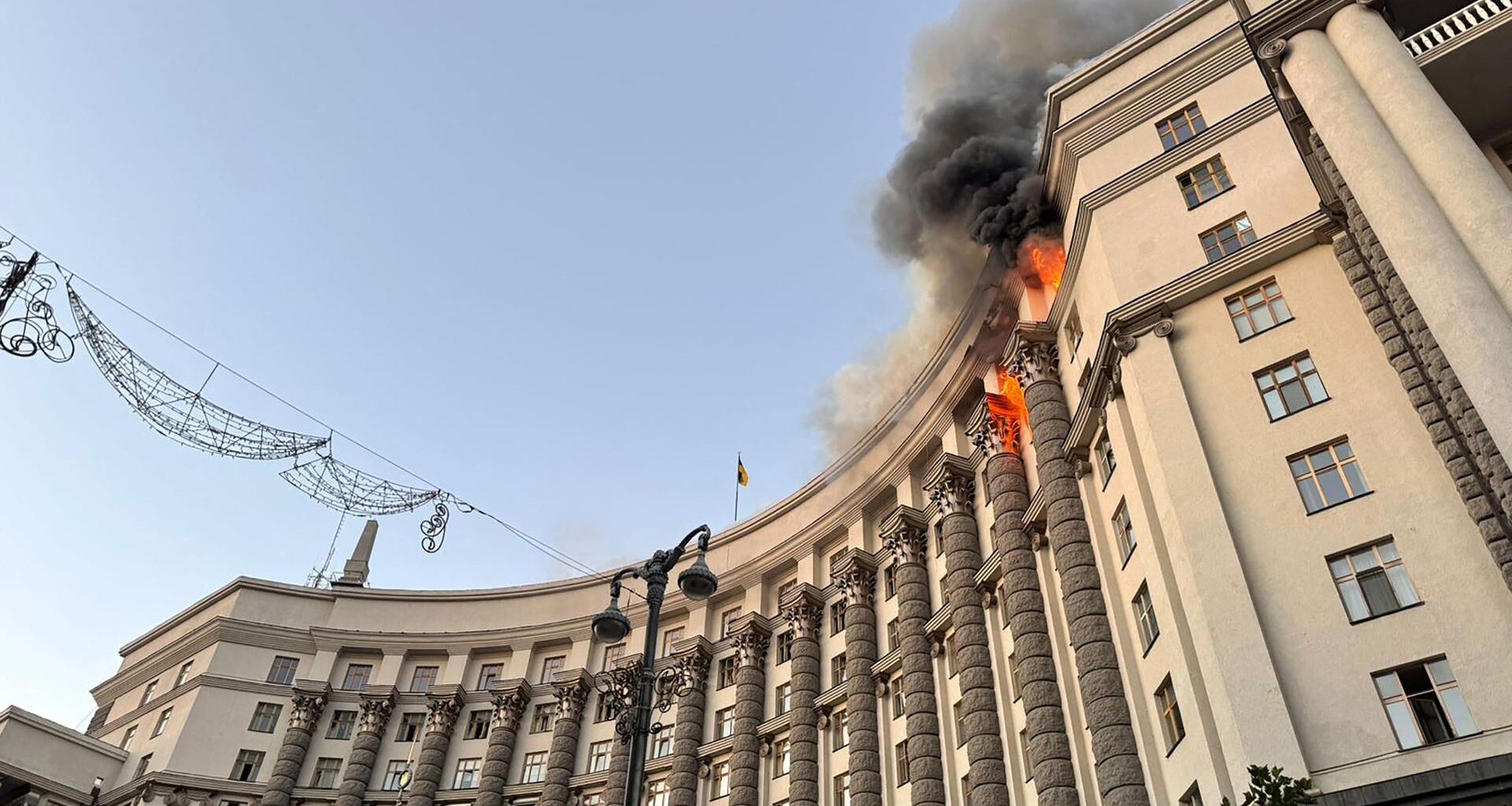Blick von unten auf die Fassade des großen Gebäudes der ukrainischen Regierung, in der obersten Etage schlagen Flammen aus mehreren Fenstern.