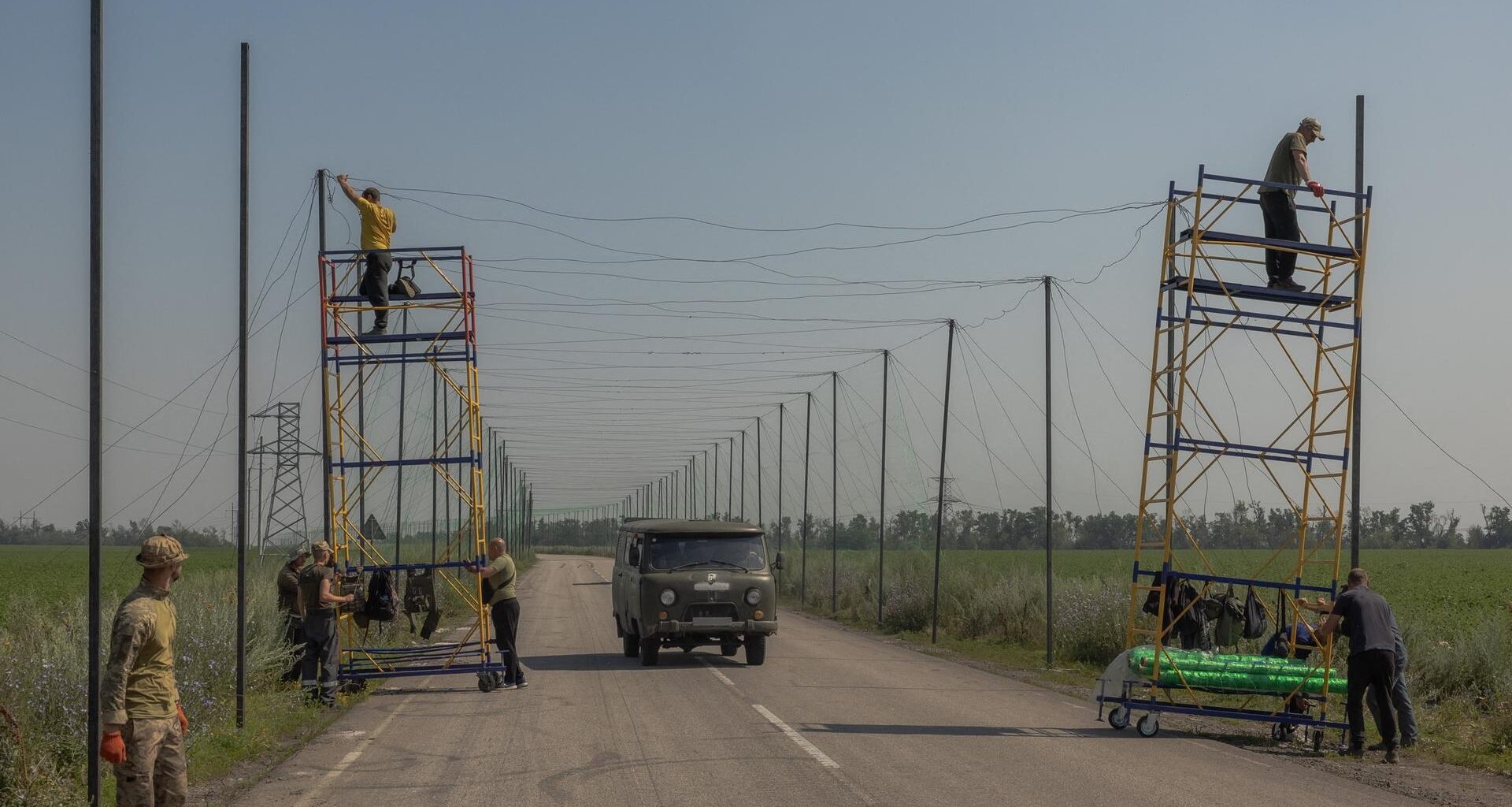 Ukrainische Arbeiter montieren Anti-Drohnen-Netze auf einer Straße.