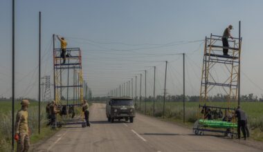 Ukrainische Arbeiter montieren Anti-Drohnen-Netze auf einer Straße.