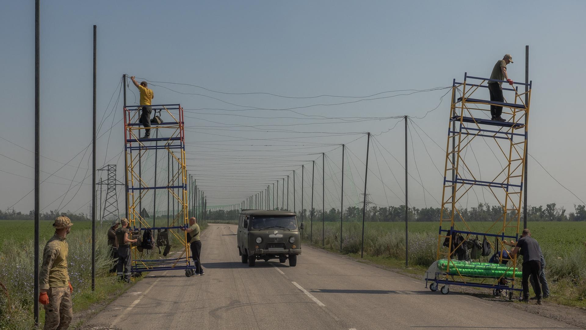 Ukrainische Arbeiter montieren Anti-Drohnen-Netze auf einer Straße.