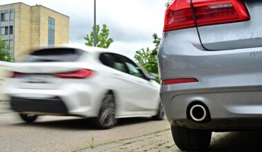 Ein Auto steht an einem Straßenrand. Groß um Bild ist der Auspuff zu sehen.