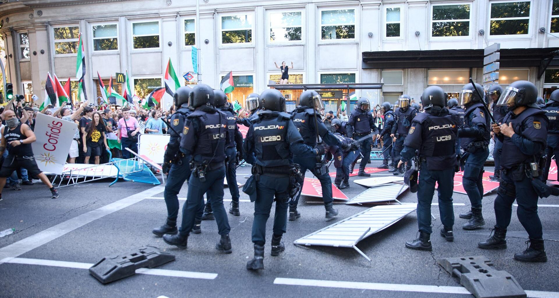 Polizisten in Einsatzkleidung steigen über umgestoßene Absperrgitter hinweg zu Demonstranten, die Palästina-Flaggen schwenken.