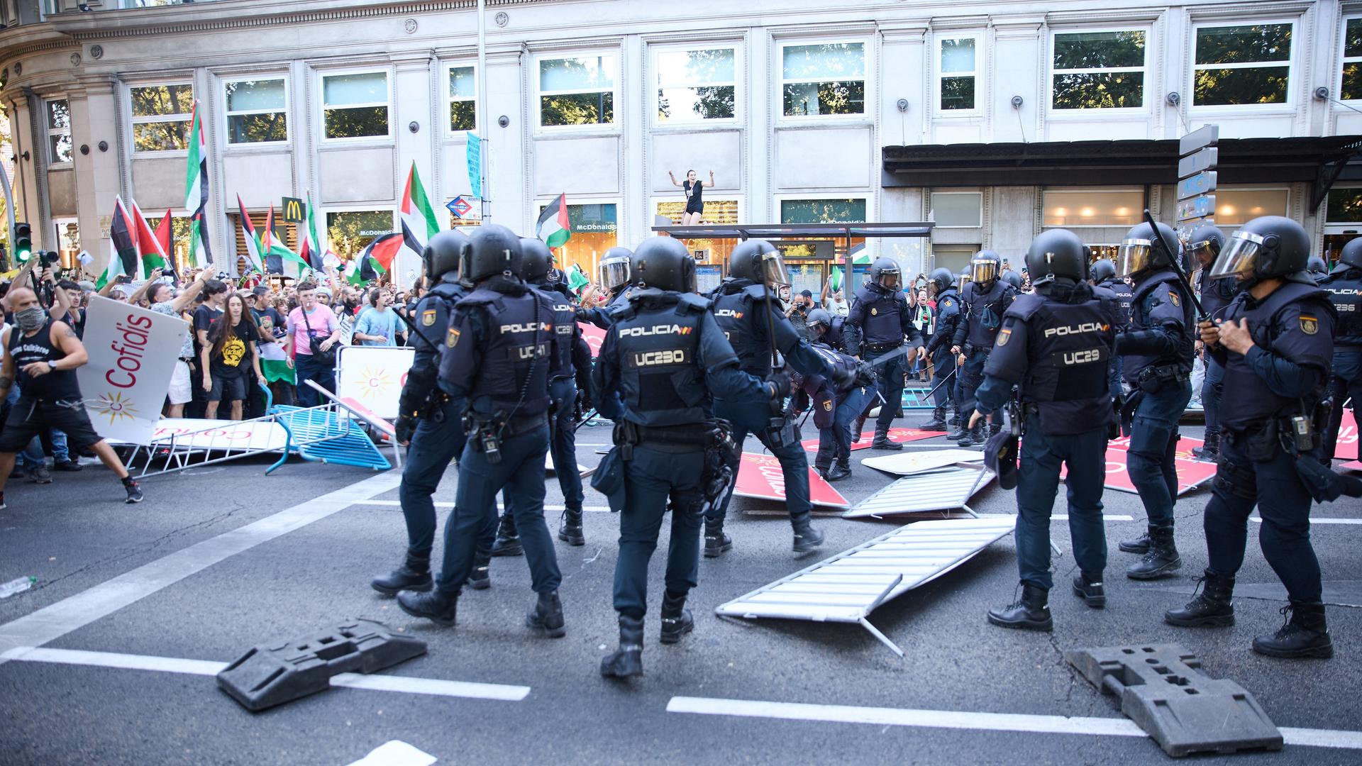 Polizisten in Einsatzkleidung steigen über umgestoßene Absperrgitter hinweg zu Demonstranten, die Palästina-Flaggen schwenken.