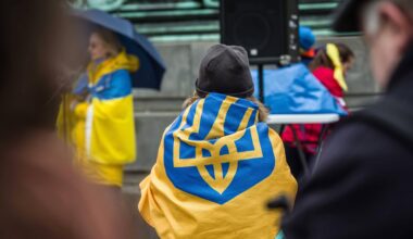 Bei einer Demonstration in München sitzt eine Frau auf der Straße und hat die ukrainische Flagge um sich geschlungen.