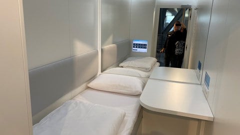 Der Blick in eine Schlafkabine am Flughafen Stuttgart mit frisch bezogenem Bett, kleinem weissen Tisch und einem Spiegel. 