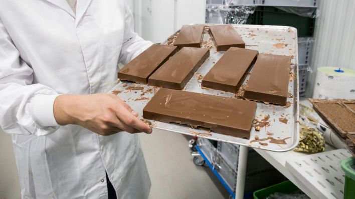 Symbolbild: Eine Frau hält ein Tablett mit Schokoladen-Riegeln in einer Fabrik in den Händen. (Quelle: dpa/Westend)