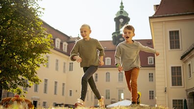 Zwei lachende Kinder rennen im Schlossinnenhof von Schloss Lichtenwalde und genießen das Kürbisfestival.