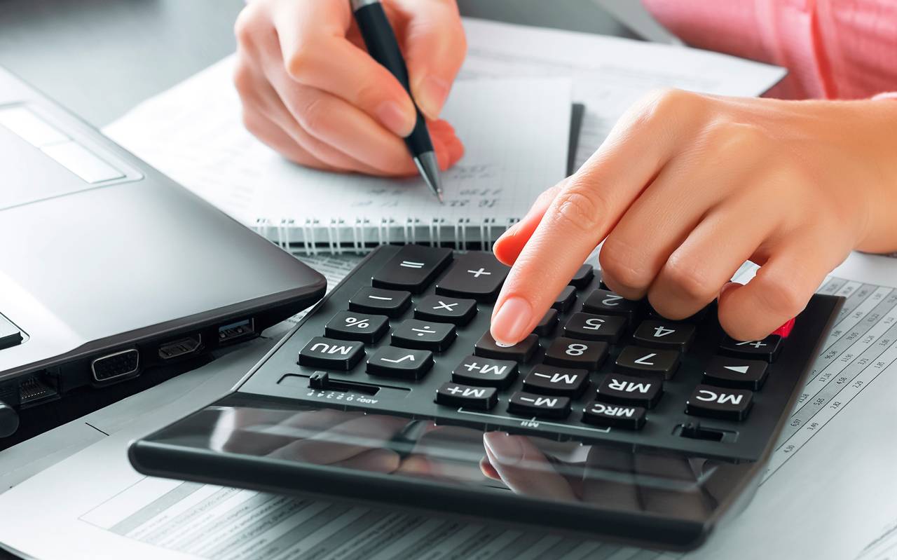 Eine Buchhalterin im Büro benutzt einen Taschenrechner und schreibt Daten in ein Notizbuch. 