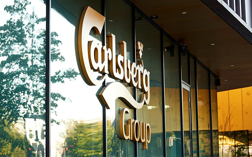 Außenansicht eines Gebäudes mit Carlsberg-Logo auf einer Glasfassade.