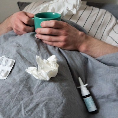 ILLUSTRATION - Ein Mann liegt mit Taschentüchern, Teetasse, Nasenspray und Tabletten im Bett (gestellte Szene). Derzeit bewegt sich die Rate akuter Atemwegserkrankungen in der Bevölkerung weiter auf einem relativ hohen Niveau im Vergleich zu früheren Jahren. +++ dpa-Bildfunk +++
