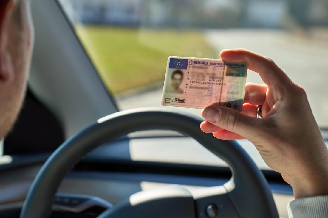 Bavaria, Germany - March 9, 2025: A young man sits in a car and holds his driver s license in front of the steering whee

