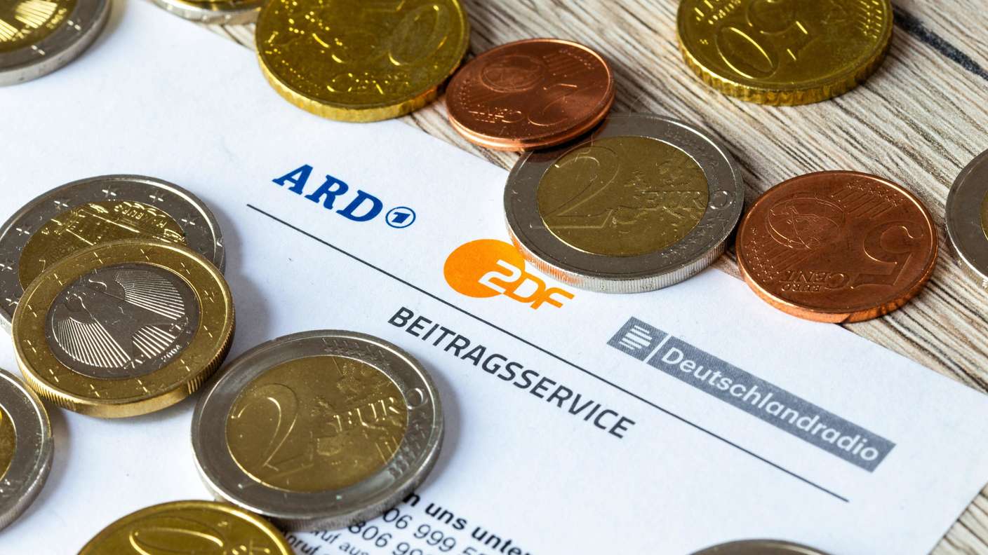Symbolbild Rundfunkbeitrag: Nahaufnahme von einem Briefbogen mit Logo von ARD, ZDF und Deutschlandradio, darauf Münzen.