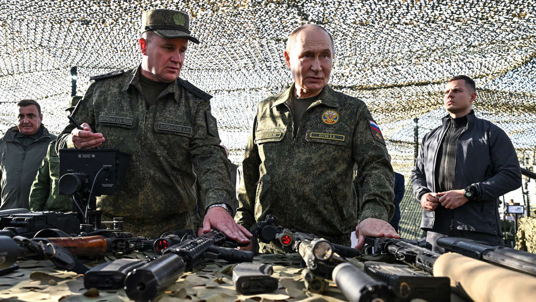 Wladimir Putin steht an eine Tisch mit Waffen