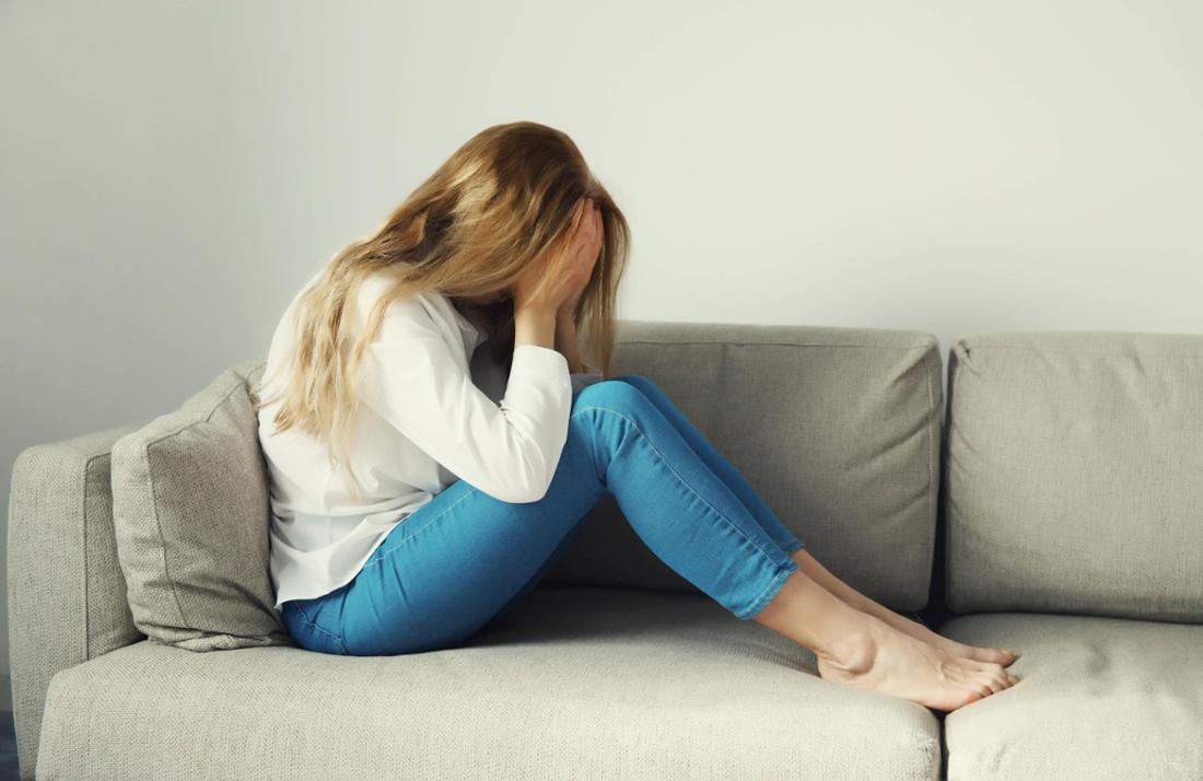 Frau sitzt auf Sofa und hält Hände in Gesicht