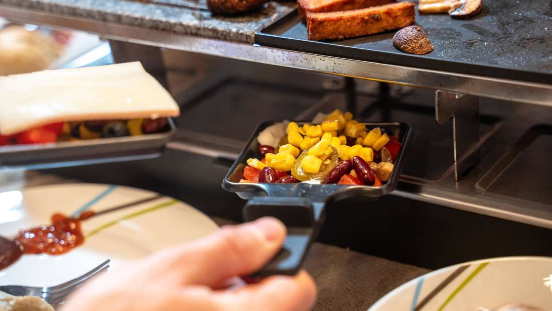 Eine Männerhand hält ein Raclette-Pfännchen.  