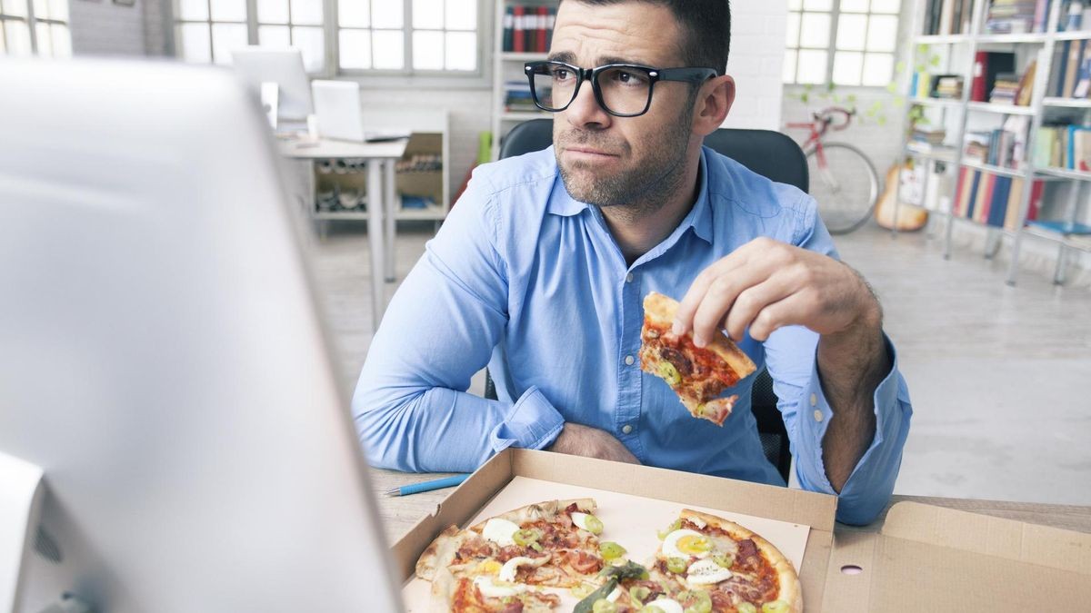 Stress im Alltag und keine Zeit, gesund zu essen? Wer sein Stresslevel senken will, kann gezielt auch bei der Ernährung ansetzen. Tired businessman eating pizza at the office