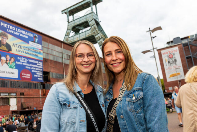 Karina Schröter und Michelle Stoll stehen vor dem Doppelbock-Förderturm auf der Zeche Ewald in Herten.