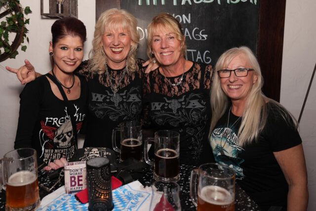 Vier Gäste der „Mauerparty“ am Donnerstagabend (2.10) mit der Coverband Seven Cent stehen an einem Tisch in Brauhaus Rütershoff in Castrop-Rauxel.