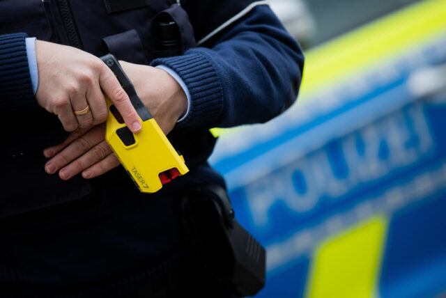 Ein Polizeibeamter steckt einen Taser in eine Tasche.