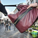 In einer gestellten Szene wird in einer Fußgängerzone einer Frau ihre rote Handtasche aus Leder entrissen.