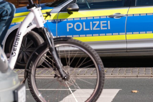 Fahrrad auf einer Straße, im Hintergrund ein Streifenwagen der Polizei.