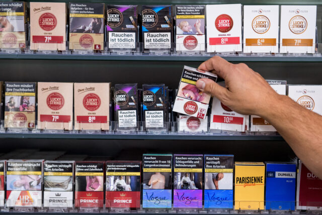 Jemand holt Zigaretten aus einem Regal.