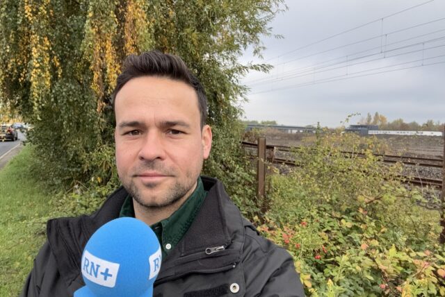 Ruhr-Nachrichten-Reporter Martin Bytomski steht mit einem Mikrofon in der Hand an der Bahnstrecke in Dortmund.