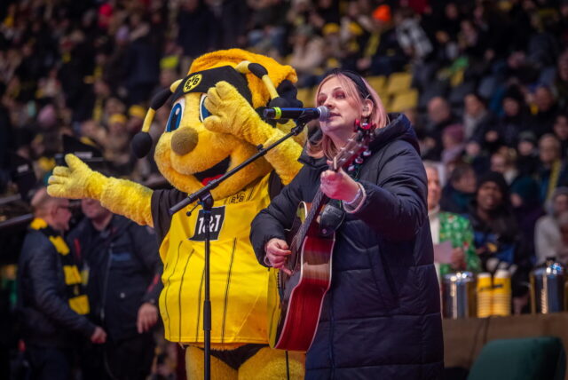 Jo Marie Dominiak singt und spielt Gitarre neben BVB-Maskottchen Emma.