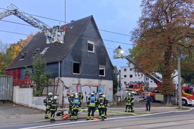Einsatzkräfte der Feuerwehr stehen vor einem Brandhaus in Dortmund.