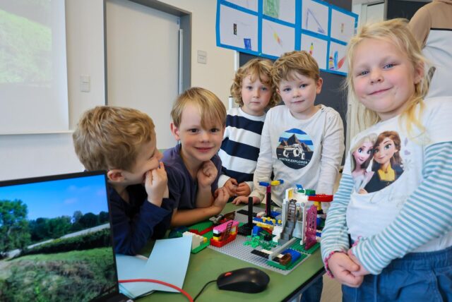 Kinder stehen vor Legosteinen.