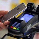Ein Smartphone (iPhone) wird an den Bezahl-Terminal an der Kasse eines Supermarktes gehalten