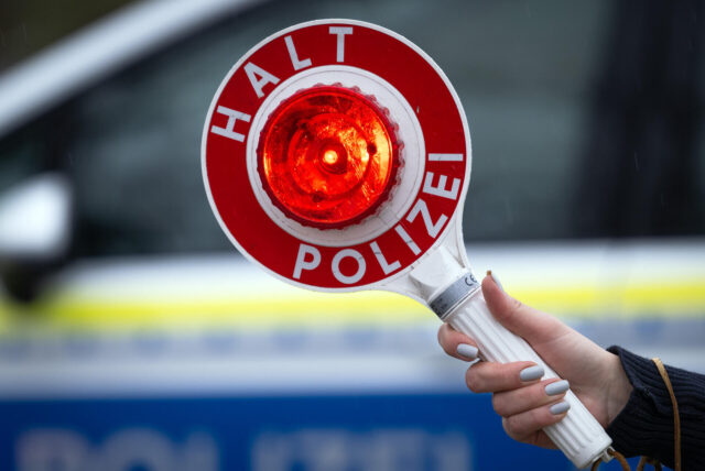 Eine Polizistin hält während einer Verkehrskontrolle eine Polizeikelle mit der Aufschrift „Halt Polizei“