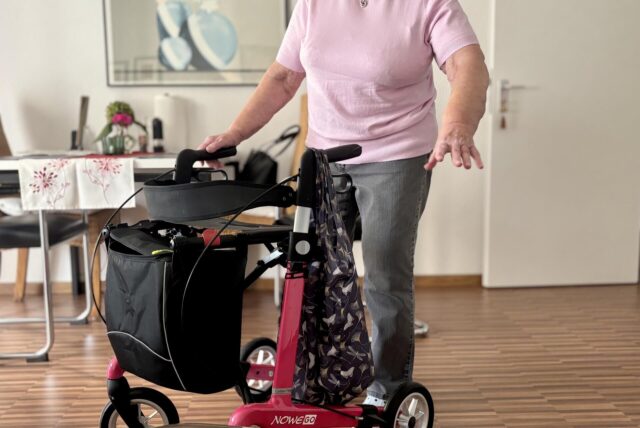 Eine Seniorin steht mit ihrem Rollator in ihrer Wohnung.