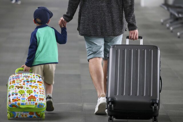 Ein Junge zieht seinen Koffer hinter sich her, während er mit seinem Vater zum Check-In geht.