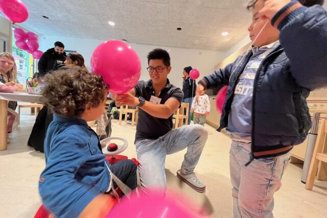 Ein Erzieher und mehrere Kinder spielen in einer Kitas mit Luftballons.