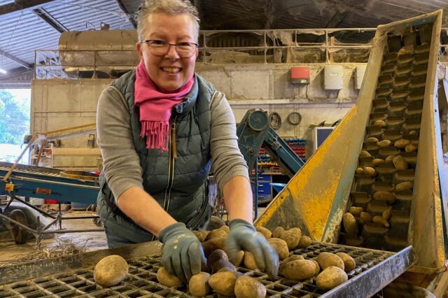 Bärbel Feldhaus sortiert Kartoffeln auf einem Rost und lächelt in die Kamera.