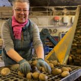 Bärbel Feldhaus sortiert Kartoffeln auf einem Rost und lächelt in die Kamera.