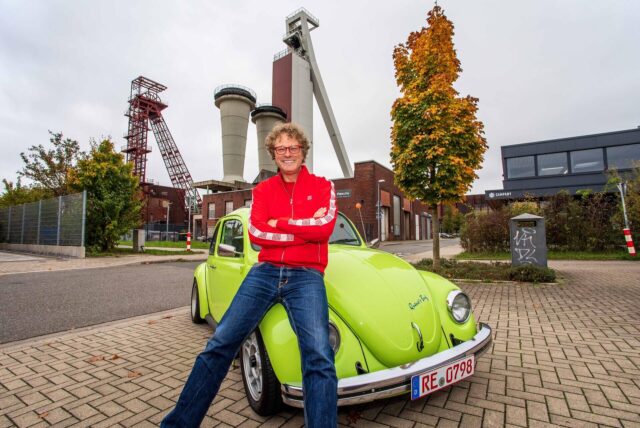 Unternehmer Dirk Krühler sitzt auf dem Kotflügel seines VW Käfers vor der ehemaligen Zeche Schlägel & Eisen in Herten.