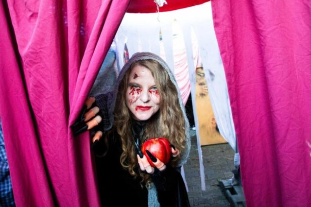 Eine gruselig geschminkte und verkleidete Frau schaut zu Halloween durch einen Vorhang