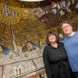 Stephanie und Mathias Mogel stehen vor einem Wandmosaik im Hausflur der umgebauten Kirche St. Johannes in Herten-Bertlich.