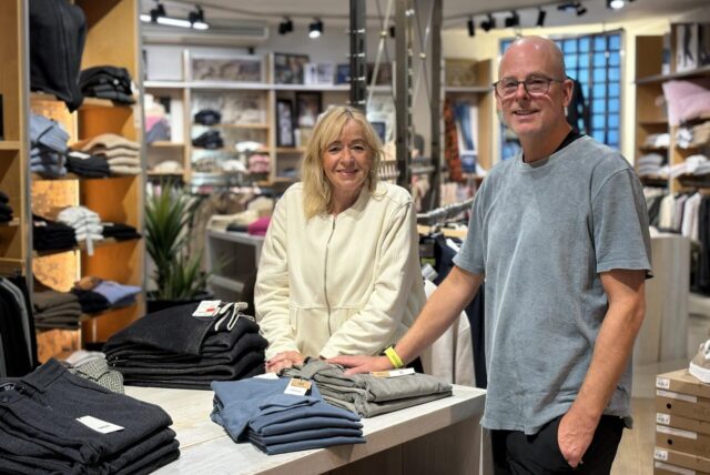 Jens Reiter und Silvia Gondrum stehen in dem Modegeschäft Reiter Fashion in der Castroper Altstadt zwischen Kleiderstapeln und Regalen.