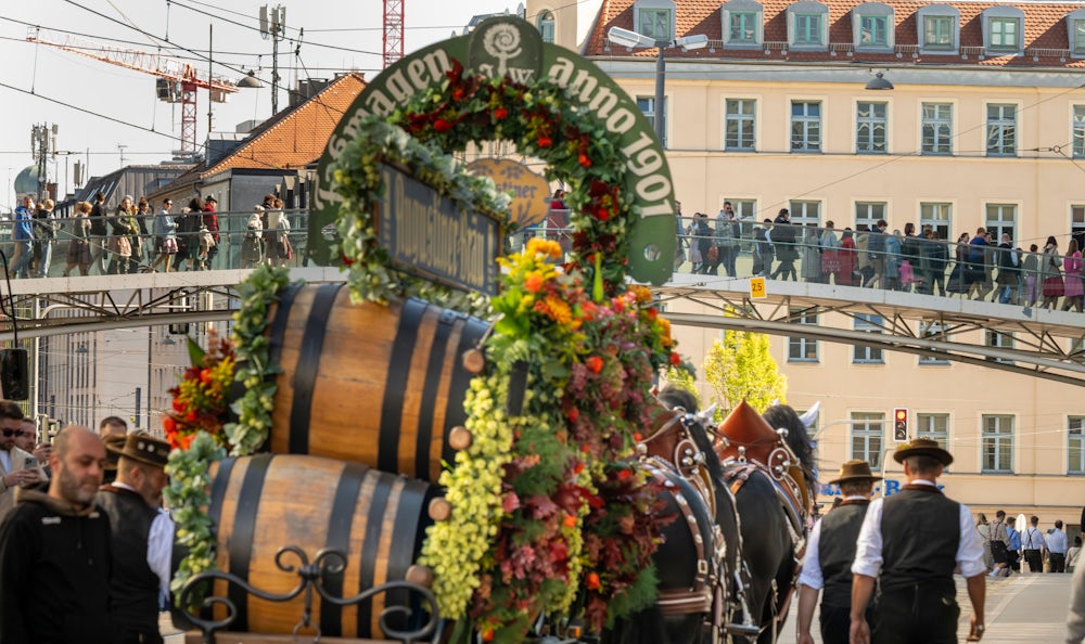 Über eine Brücke drängen die Besucher zur Theresienwiese, während die Pferdekutsche einer Brauerei  mit Fässern beladen zum Festgelände steuert.